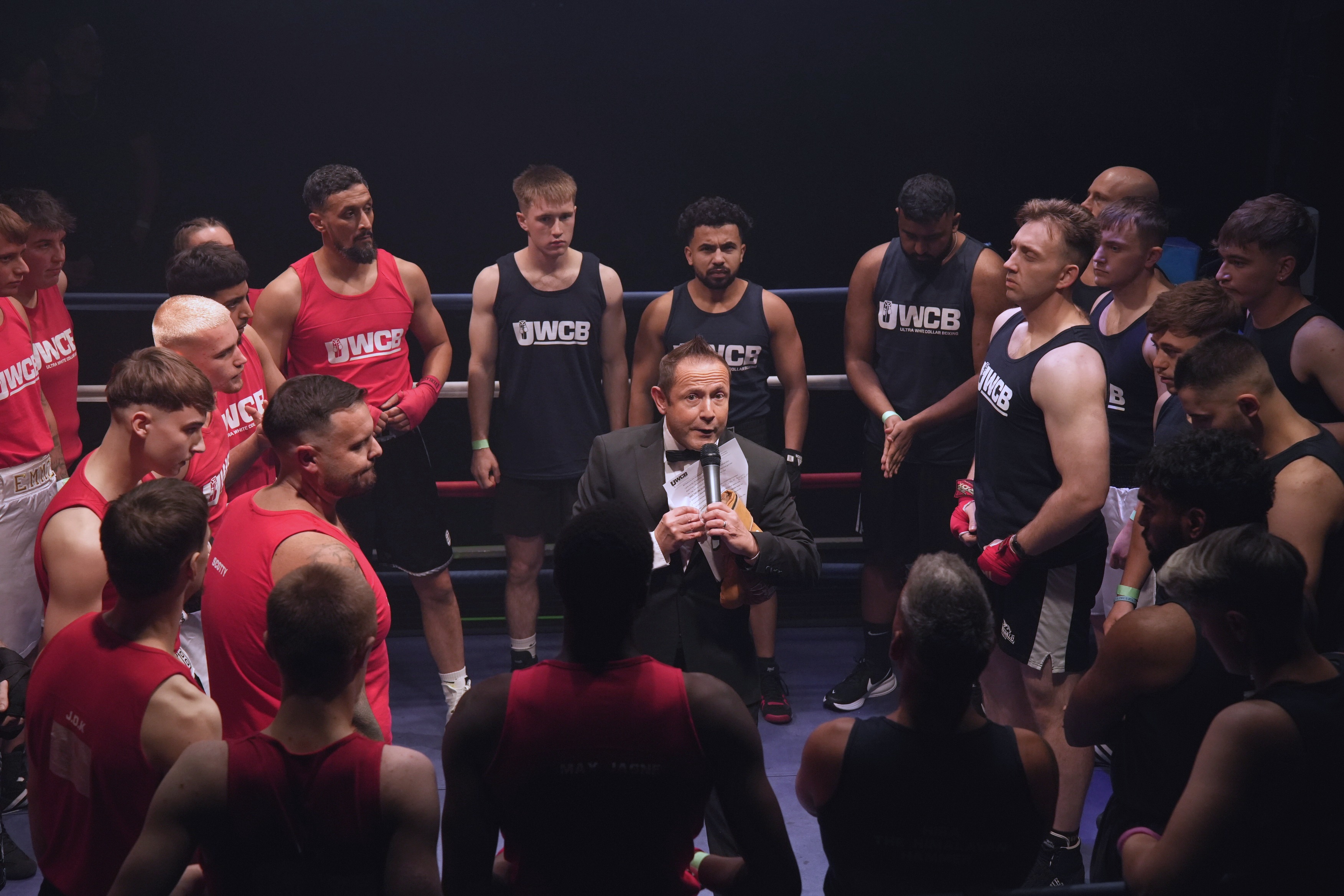 Nick Mummery surrounded by red and black team fighters in the ring